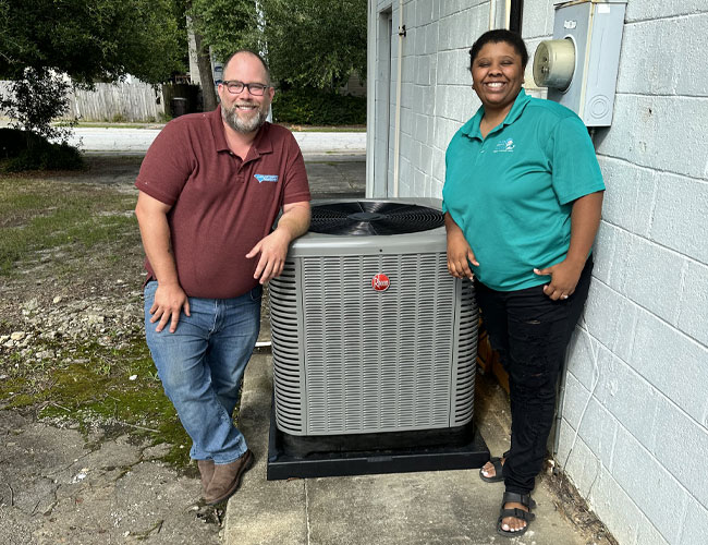 Carolina Comfort tech standing next to a brand new Rheem HVAC system and a very happy customer